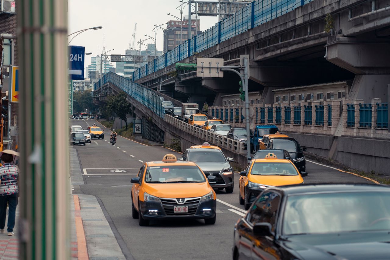 ours-journey Yellow taxis and vehicles navigating an urban street under an overpass.